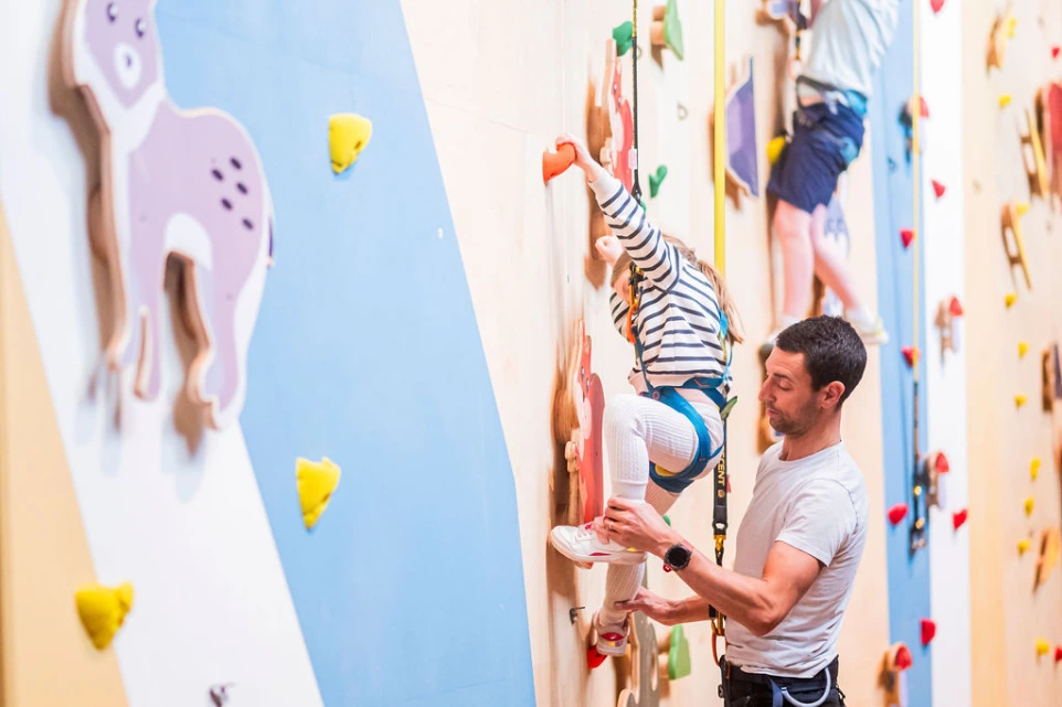Un enfant pratique l’escalade en salle avec l’aide d’un adulte