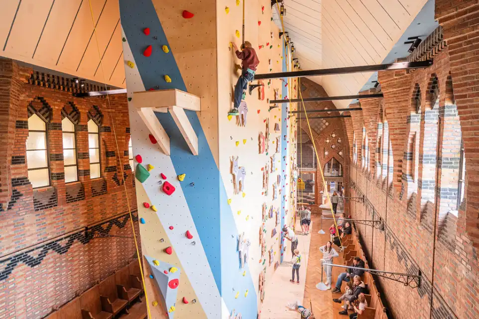 Des enfants grimpent sur un mur d’escalade coloré dans une salle intérieure lumineuse