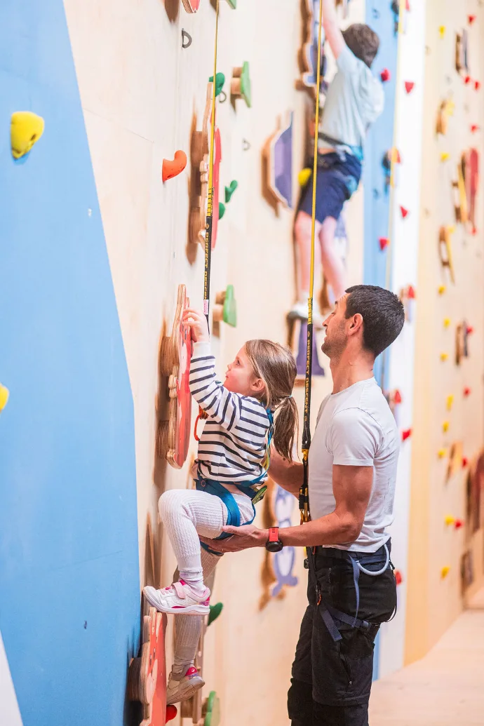 Un enfant pratique l’escalade en salle avec l’aide d’un adulte